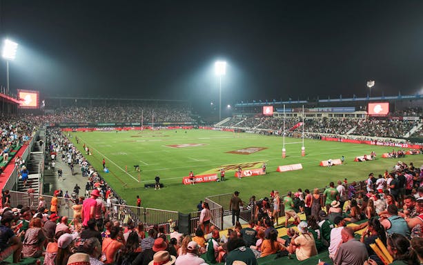 Crowd watching a rugby match at night during the Emirates Dubai 7's tournament.