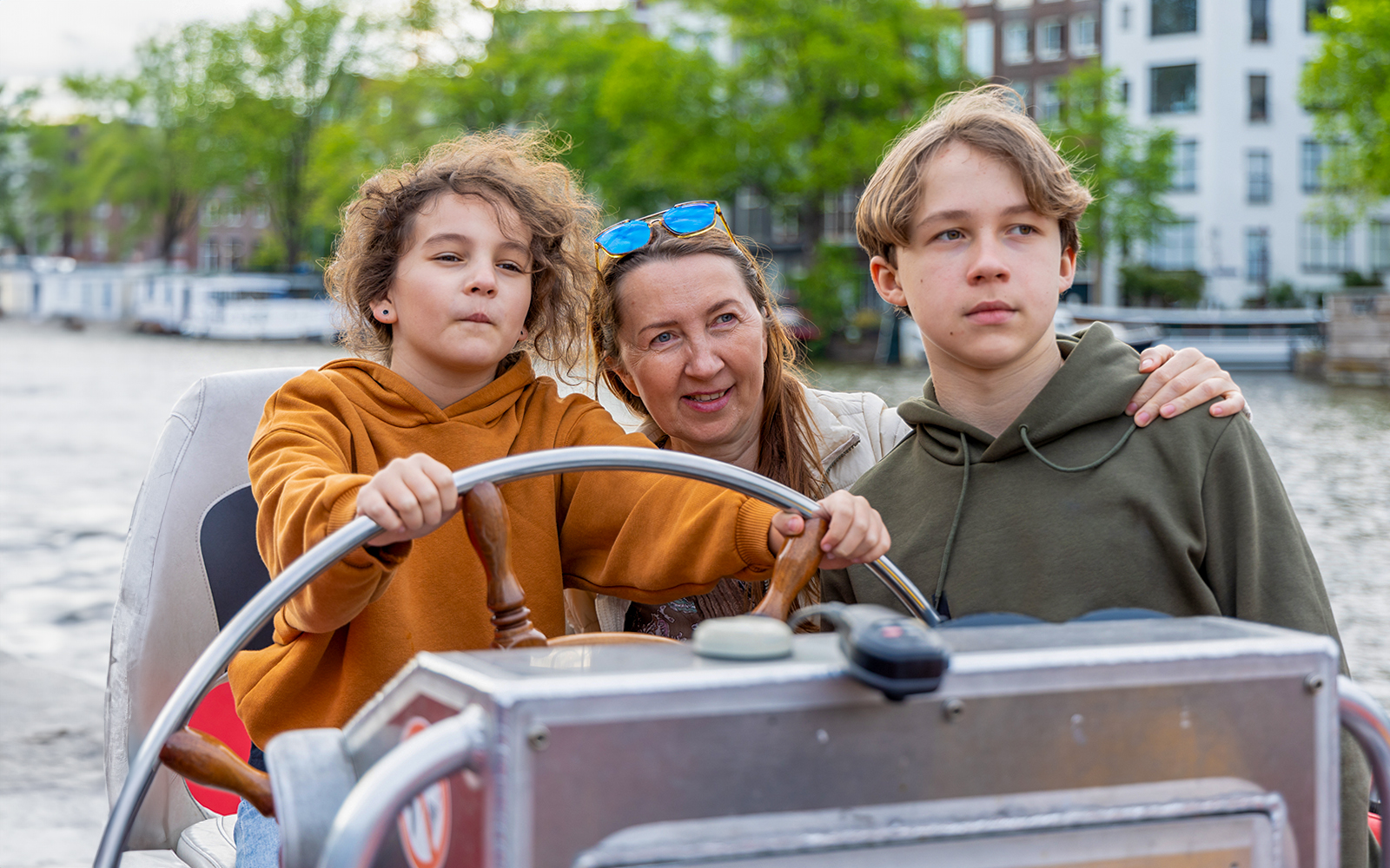 Passengers enjoying a cruise, child steering the boat with family on a scenic waterway.