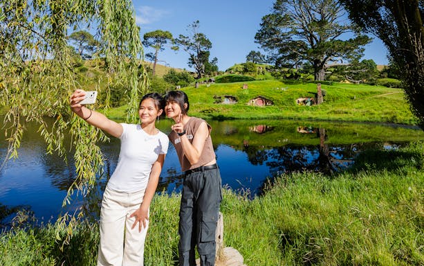 Girls taking a selfie with Hobbiton movie set hobbit houses in the background.