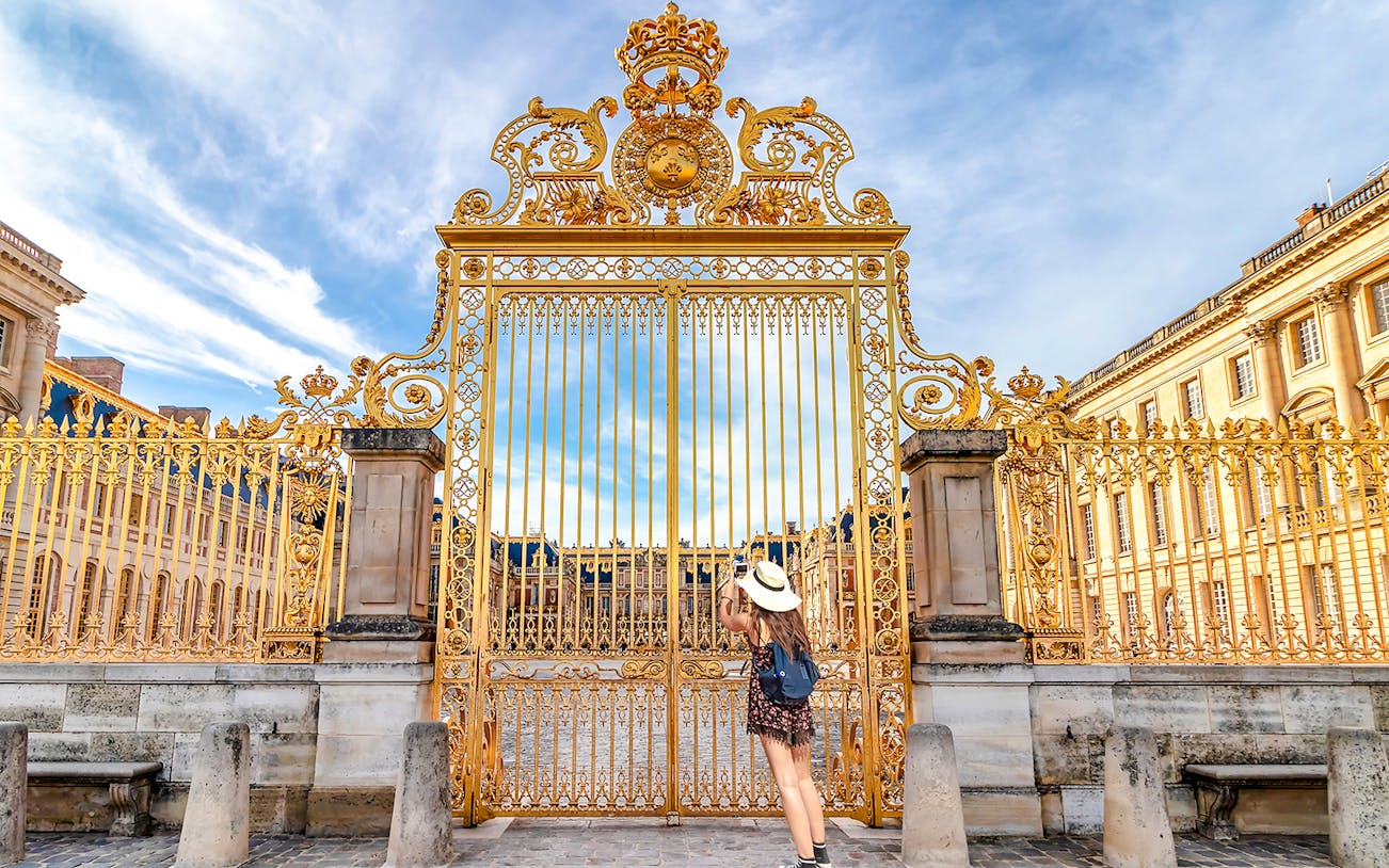 Golden gate at Versailles Palace facade, Paris, with visitor admiring.