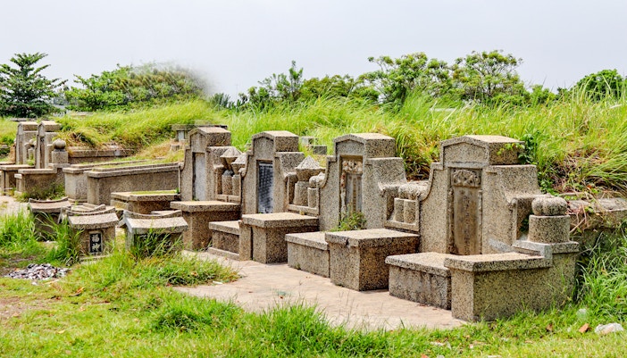 Stone tombstones at Bukit Brown Chinese cemetery surrounded by greenery.