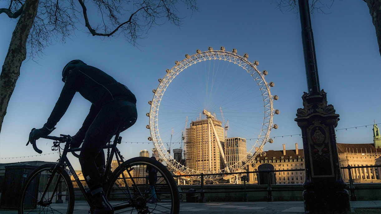 Cyclists riding along the Thames River with the London Eye in the background.