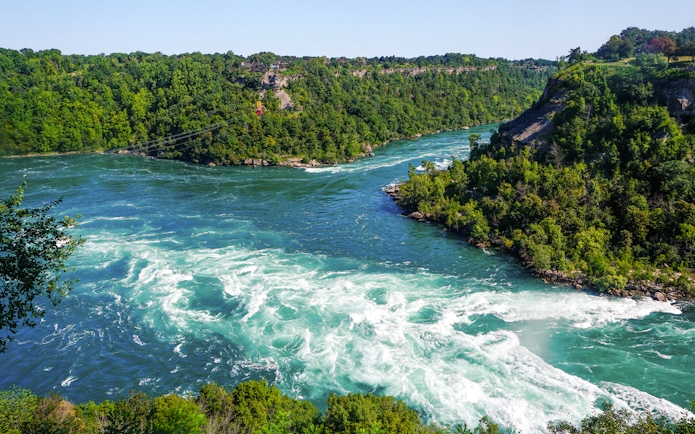 Niagara Whirlpool along the Niagara River surrounded by lush green forests.