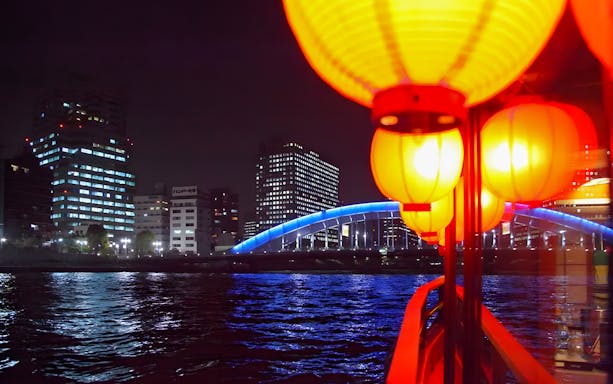 Yakatabune boat with lanterns on Tokyo Bay at night, city skyline and bridge in view.
