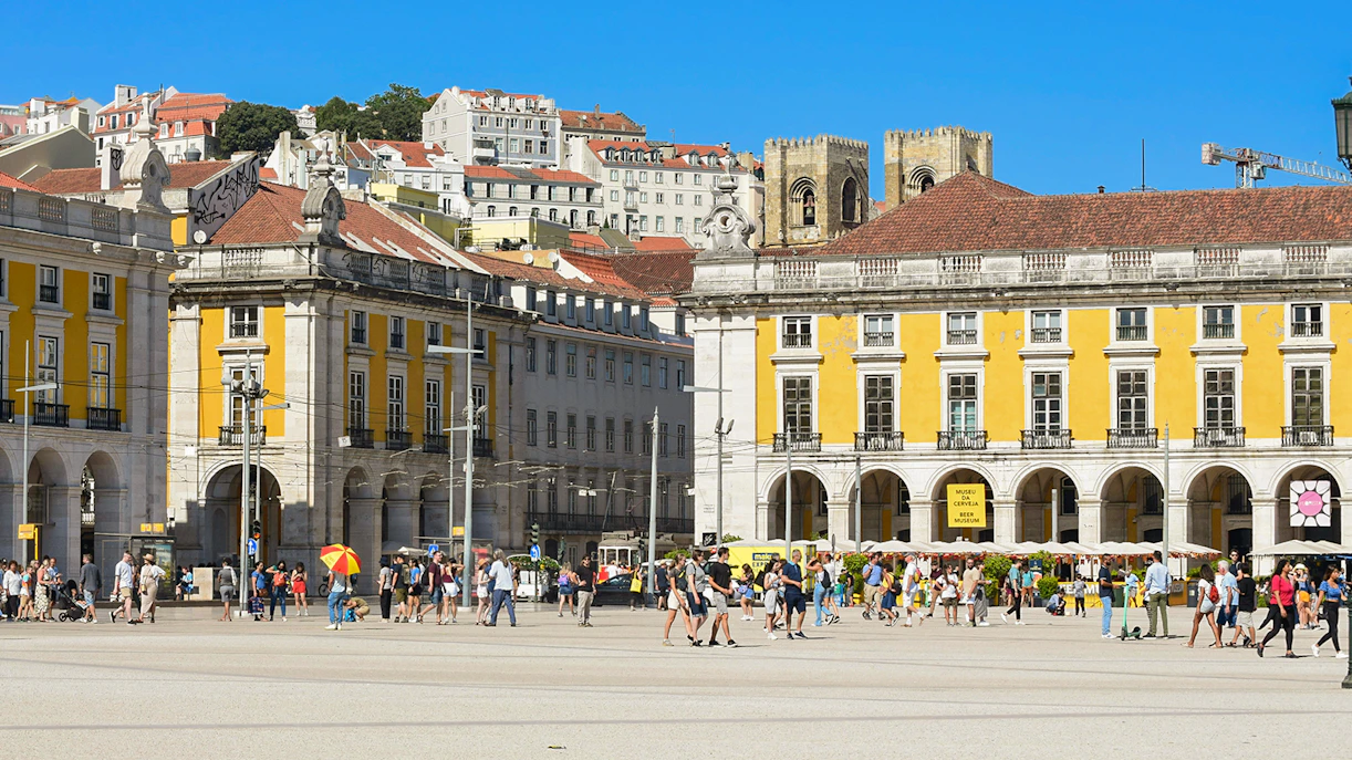 Crowd at Praça do Comércio in Lisbon with historic yellow buildings in the background.
