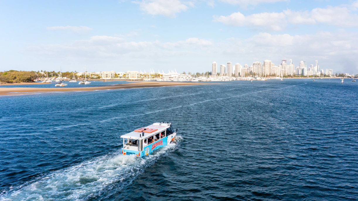 Aquaduck vehicle cruising on a river with city skyline in the background.