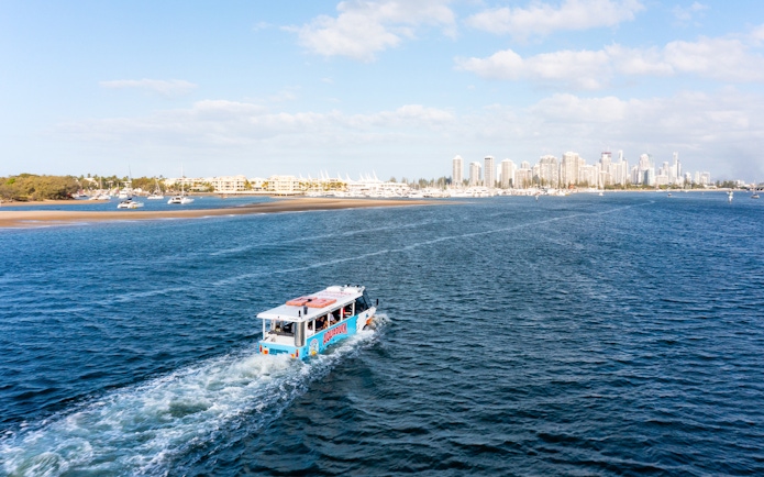 Aquaduck vehicle cruising on a river with city skyline in the background.