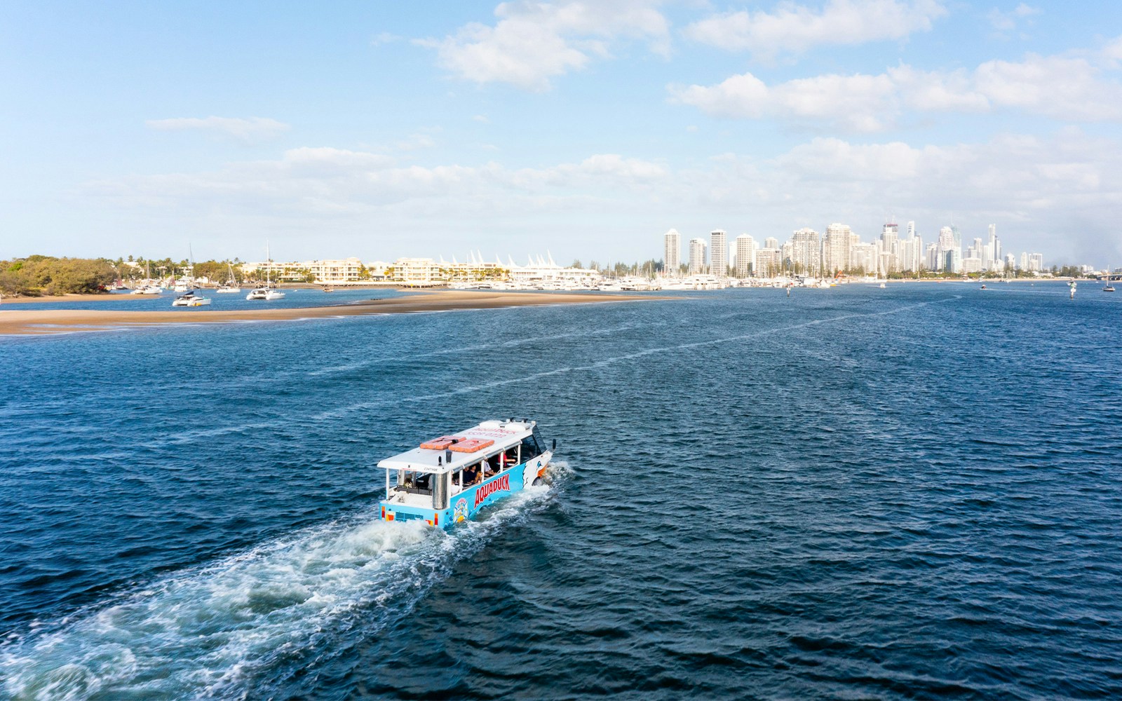 Aquaduck vehicle cruising on a river with city skyline in the background.