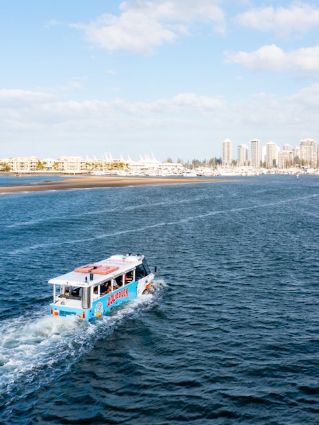 Aquaduck vehicle cruising on a river with city skyline in the background.