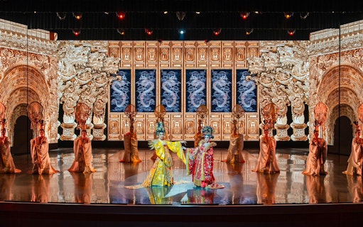 Traditional Chinese performance with ornate costumes and dragon backdrop at The Colosseum.