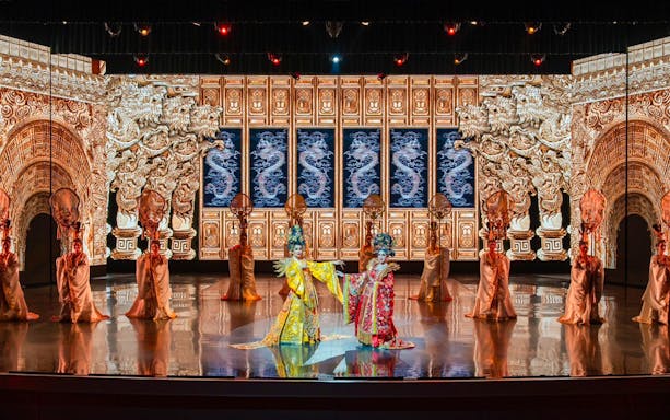 Traditional Chinese performance with ornate costumes and dragon backdrop at The Colosseum.