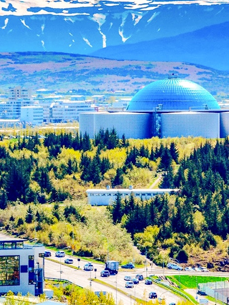 Perlan Museum with forested surroundings in Reykjavik, Iceland, under a mountainous backdrop.