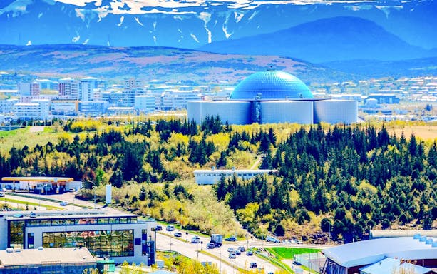 Perlan Museum with forested surroundings in Reykjavik, Iceland, under a mountainous backdrop.