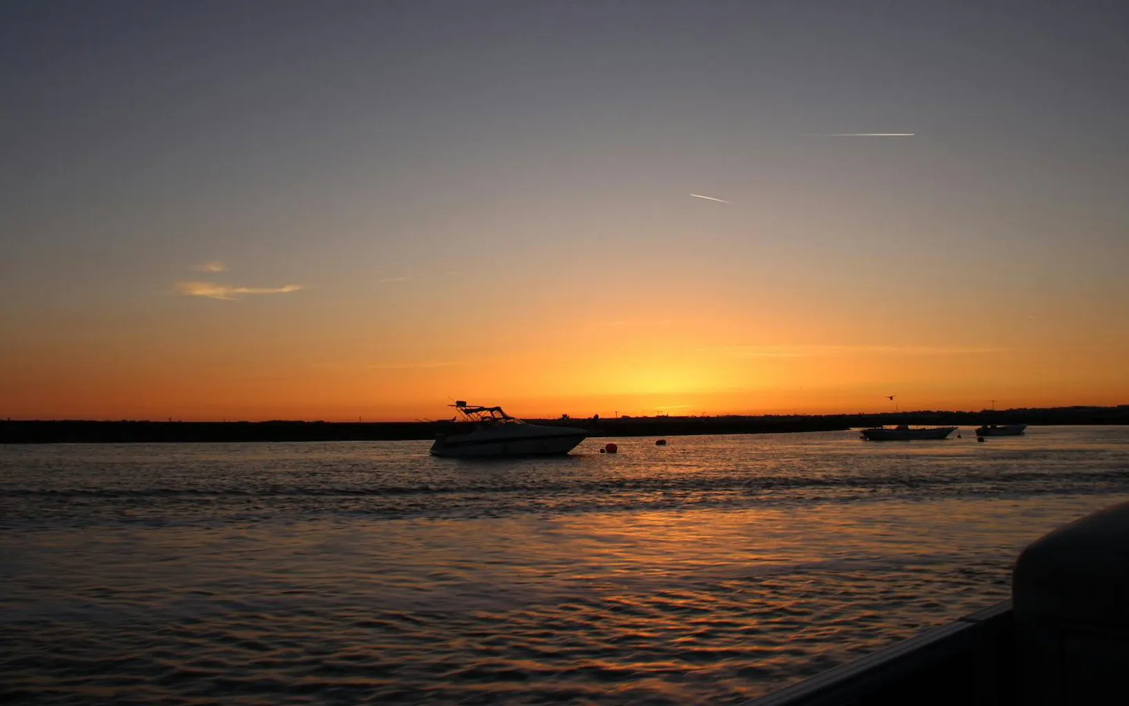Boat on Ria Formosa at sunset with orange sky and calm waters.