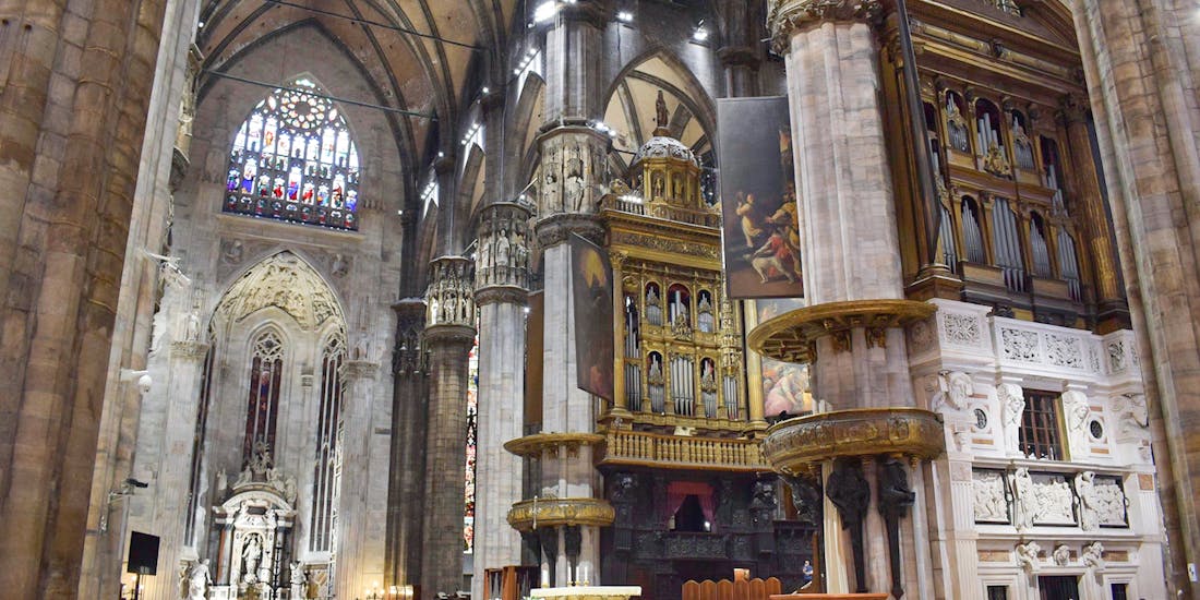 Interior view of Duomo Milan Cathedral featuring ornate columns and stained glass windows.