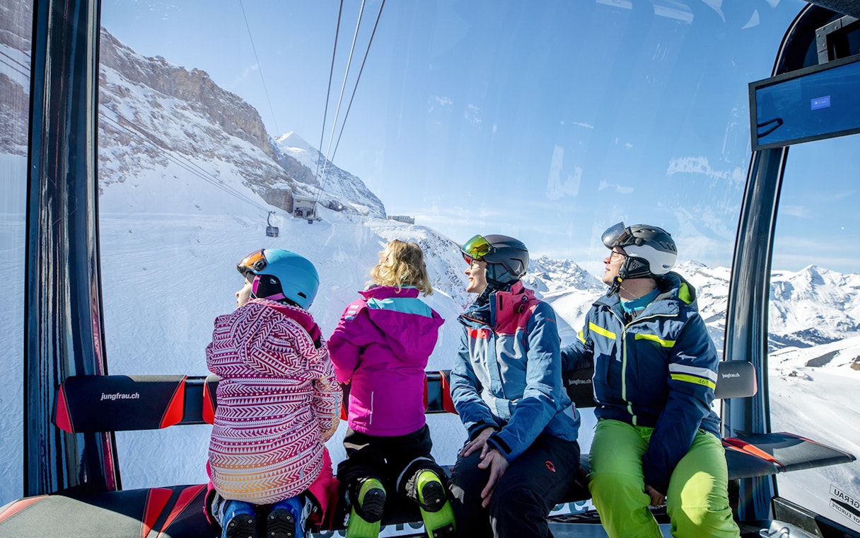 Family riding Eiger Express cable car with snowy Swiss Alps view.