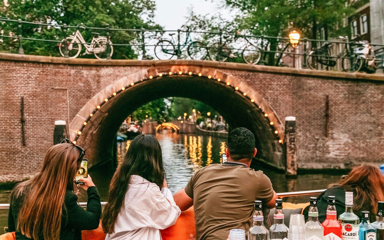 Luxury boat cruising Amsterdam canals at sunset with passengers enjoying onboard bar.