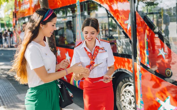 HOHO bus crew assisting woman with route map near red tour bus.