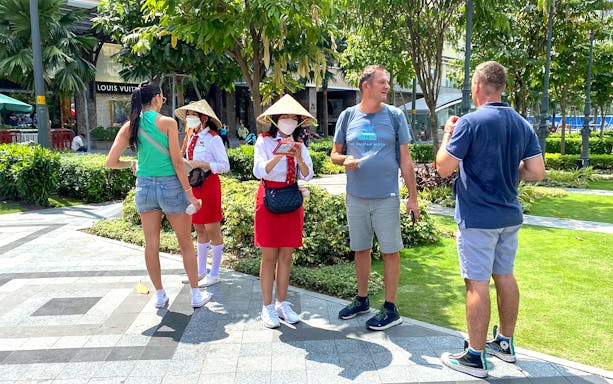Tourists receiving brochures from guides in traditional hats, Saigon Hop-on Hop-Off Sightseeing Tours.