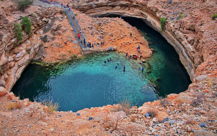 Visitors swimming in the turquoise waters of Bimmah Sinkhole, Oman.