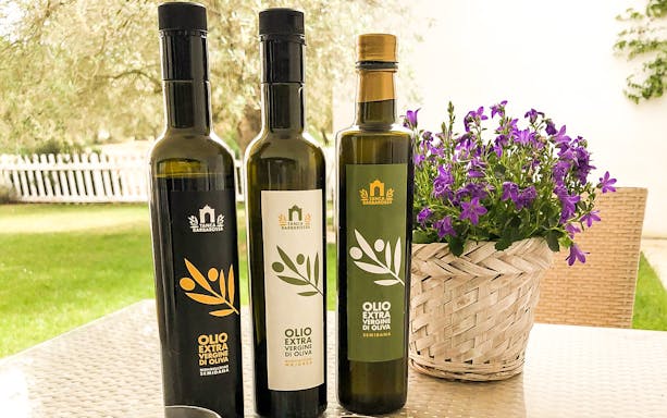 Bottles of extra virgin olive oil on a table with purple flowers, Oristano.