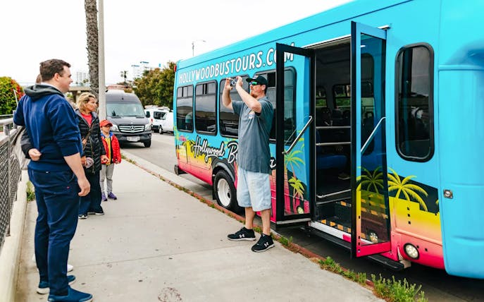 Man photographing group by Hollywood Bus Tours vehicle in Los Angeles.