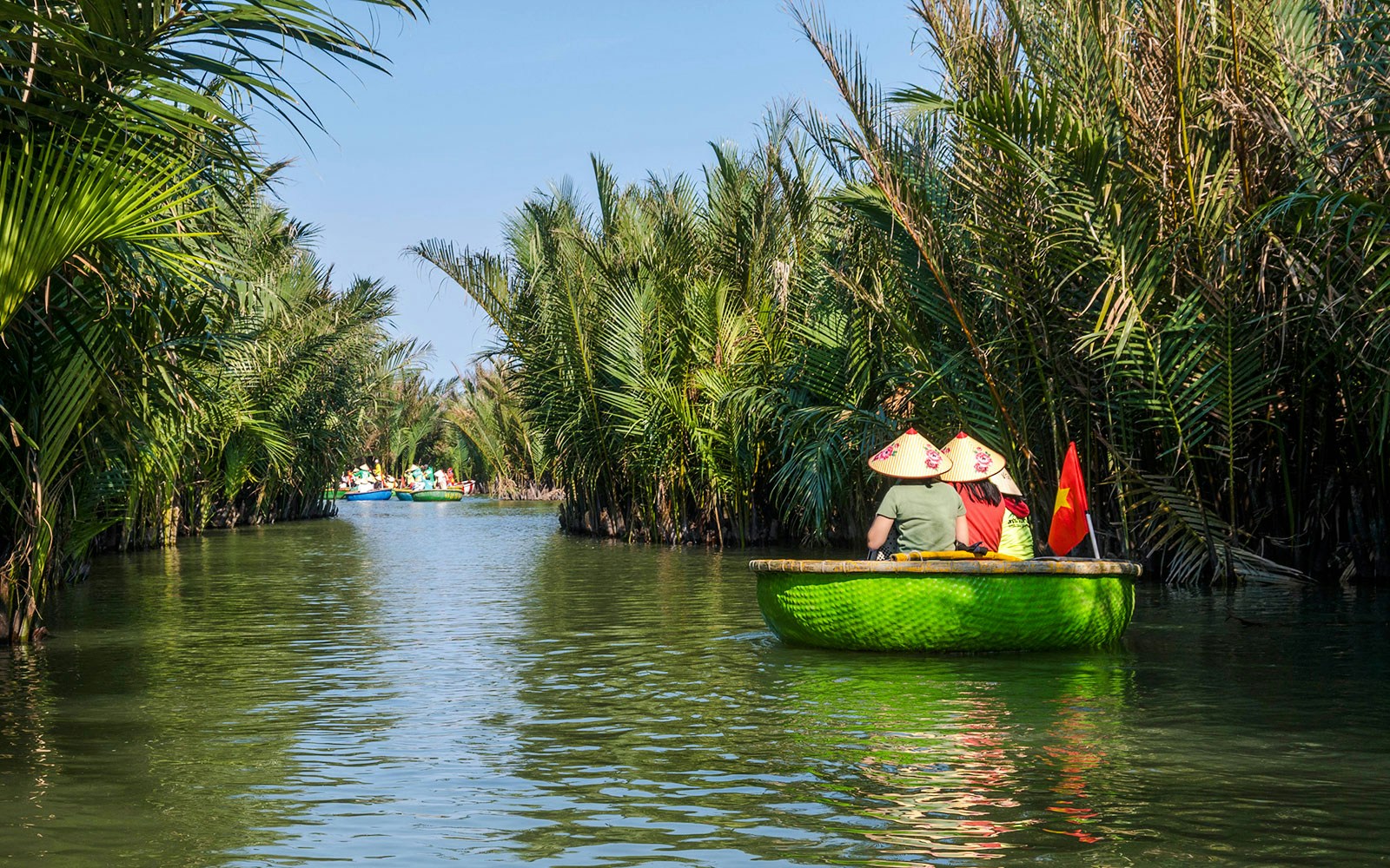 Tourists in basket boats navigating through a lush coconut forest in Vietnam.