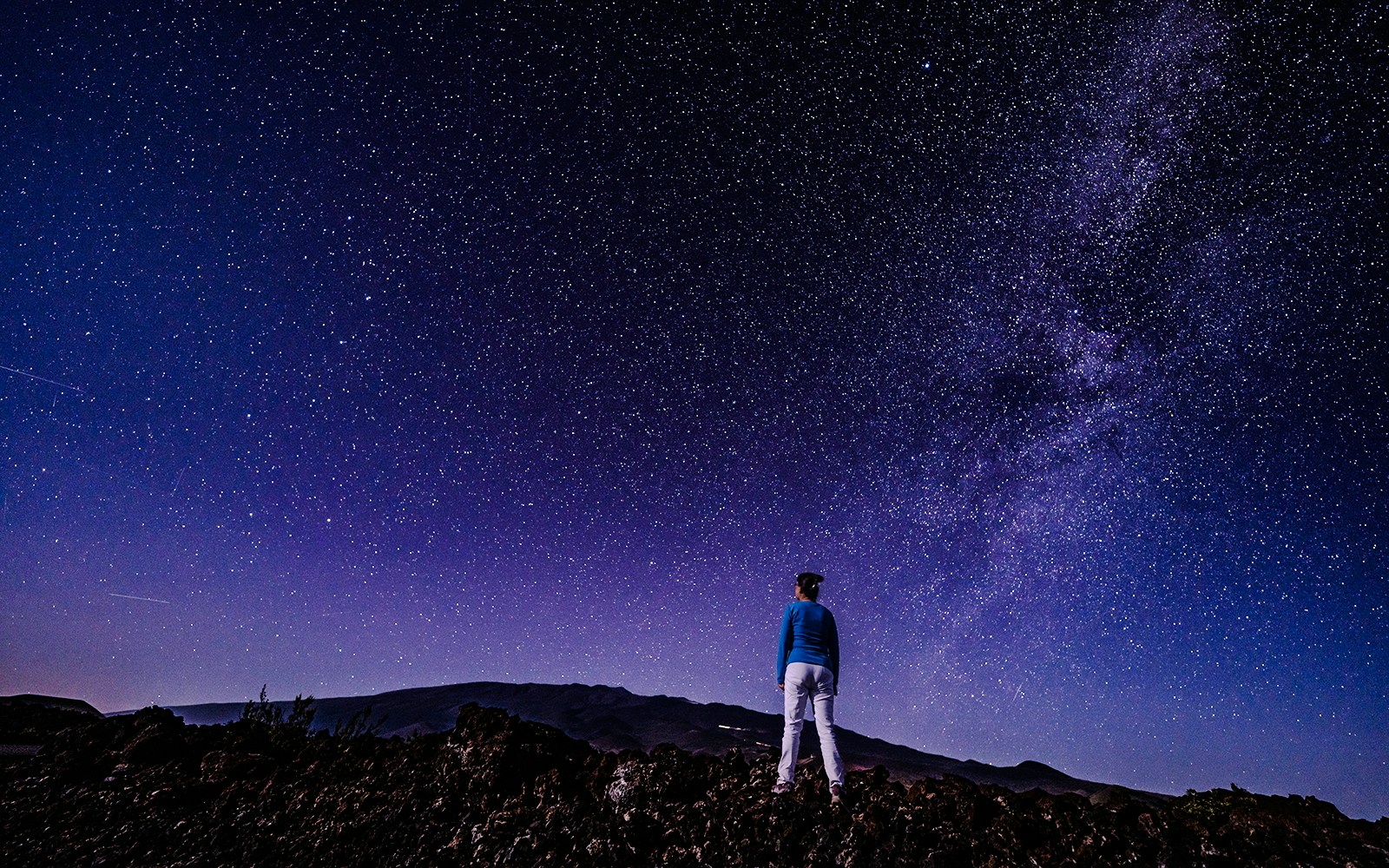 Person stargazing at Mauna Loa Observatory Road under a starry sky, Big Island, Hawaii.