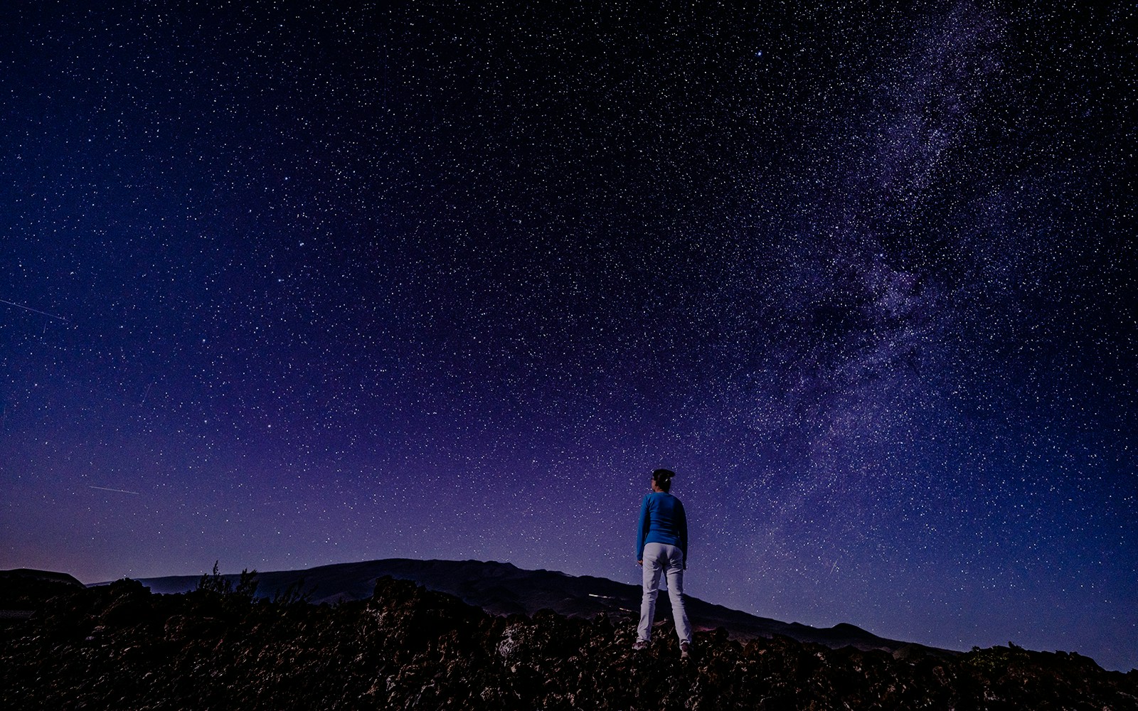 Person stargazing at Mauna Loa Observatory Road under a starry sky, Big Island, Hawaii.