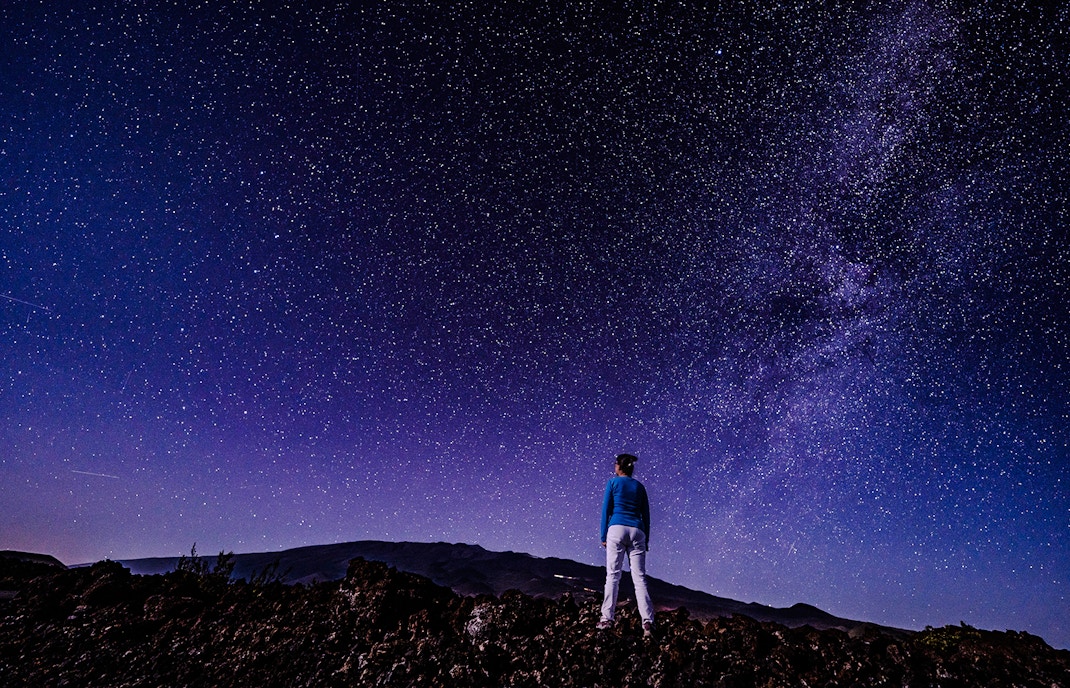Person stargazing at Mauna Loa Observatory Road under a starry sky, Big Island, Hawaii.