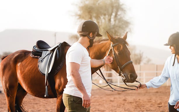 Horseback riding at Mleiha Arena with two riders preparing a horse.