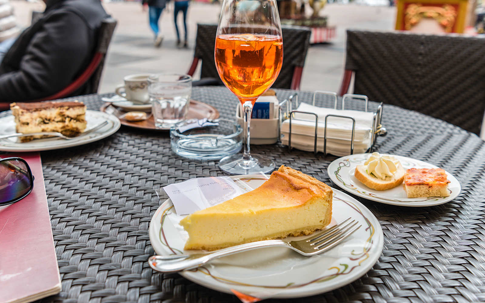 Slice of tiramisu and cheesecake on a cafe table in an outdoor setting.
