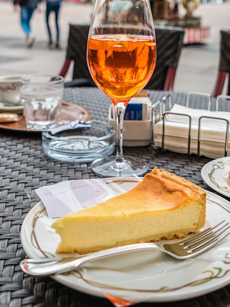 Slice of tiramisu and cheesecake on a cafe table in an outdoor setting.