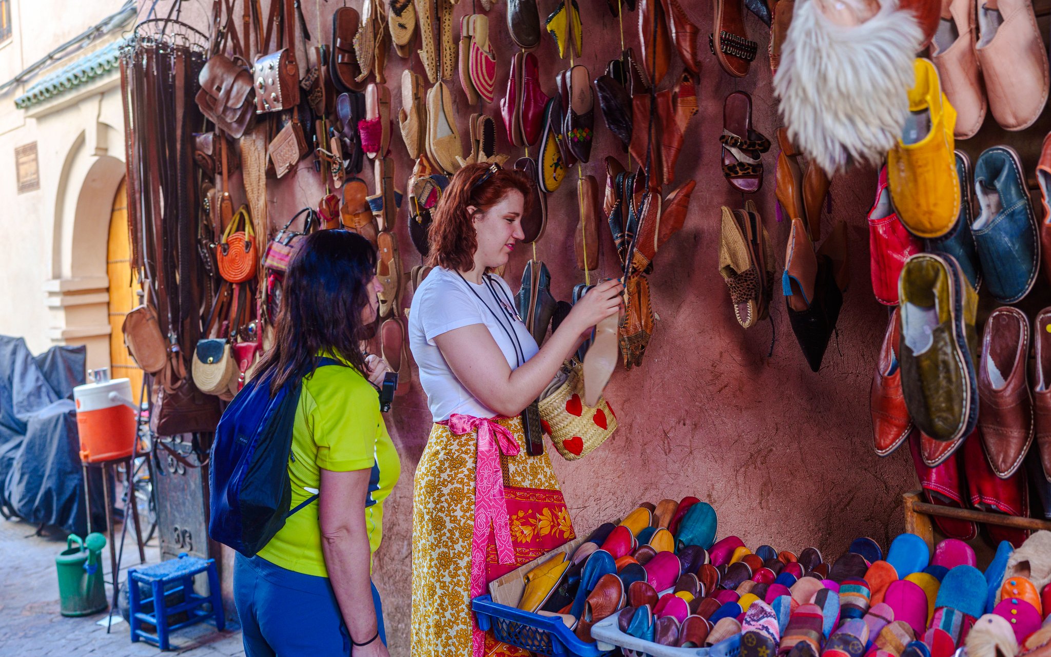 Visitors browsing colorful slippers in Marrakech Souks, Morocco.