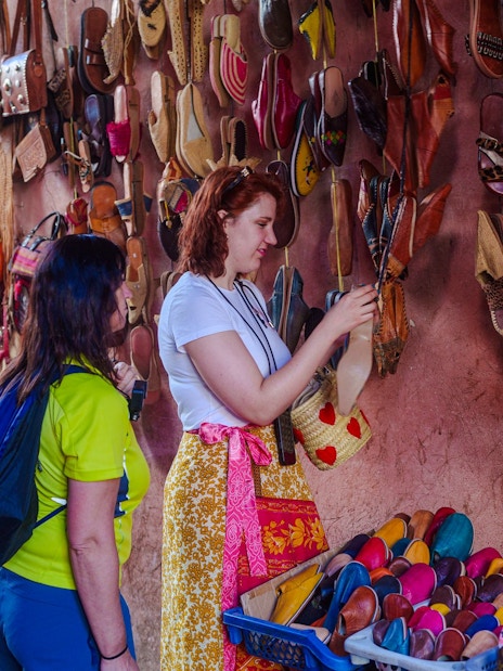 Visitors browsing colorful slippers in Marrakech Souks, Morocco.