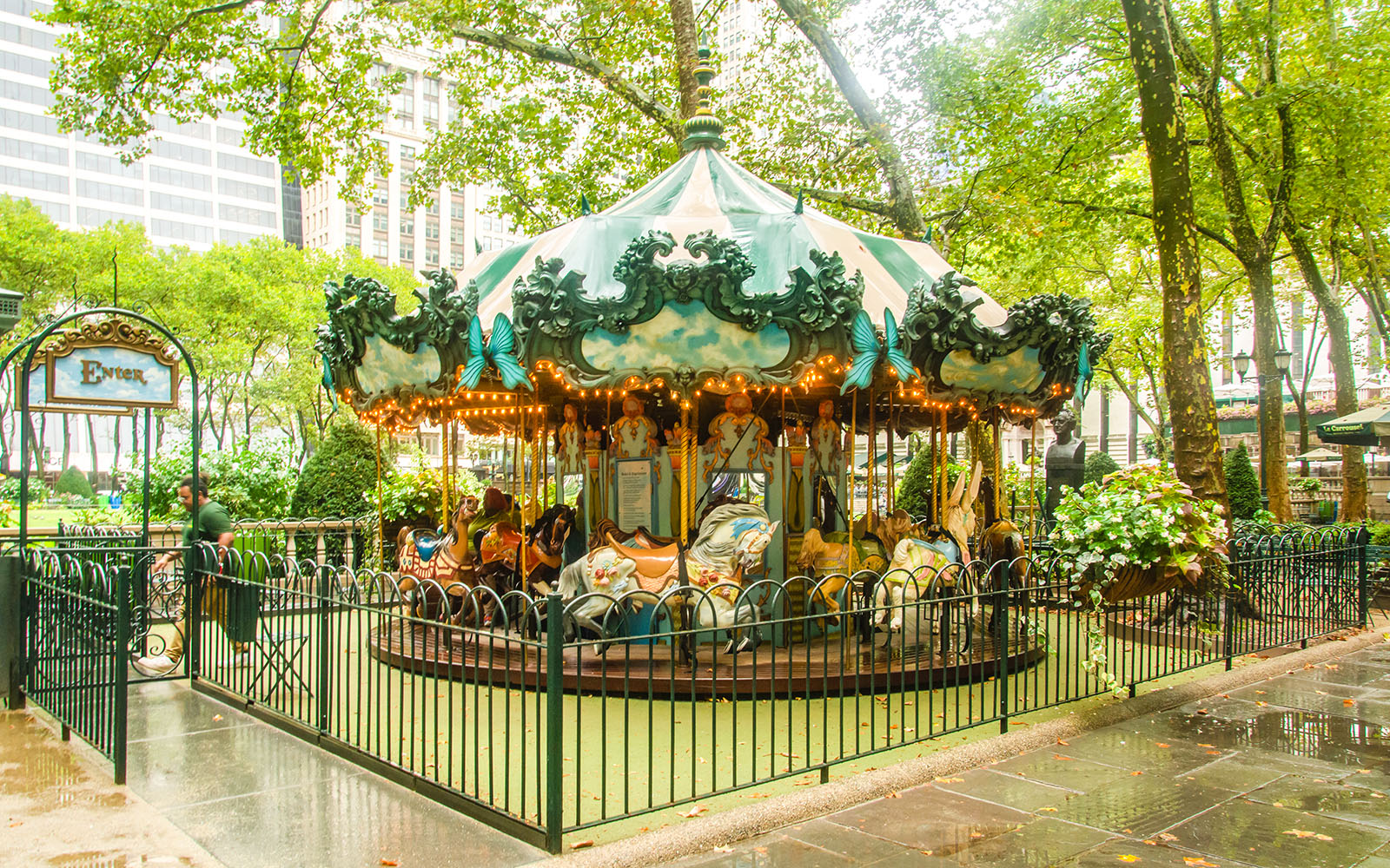 Bryant Park carousel surrounded by trees and city buildings in New York City.