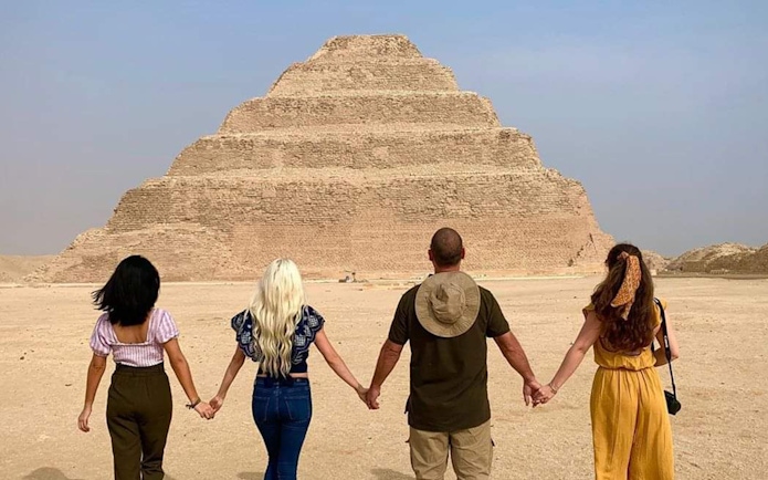 Tourists holding hands in front of the Step Pyramid at Saqqara, Egypt.