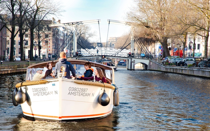 Open boat cruise on Amsterdam canal with people enjoying the view of a drawbridge.
