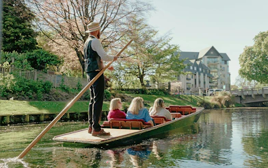 Punting on the Avon River in Christchurch with a guide steering the boat past scenic riverside views.