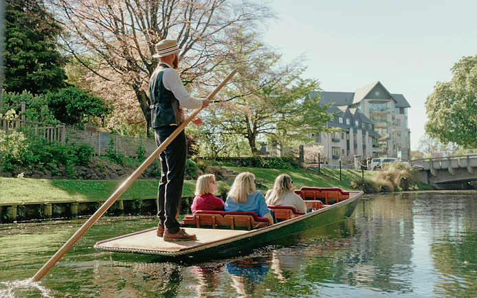 Punting on the Avon River in Christchurch with a guide steering the boat past scenic riverside views.