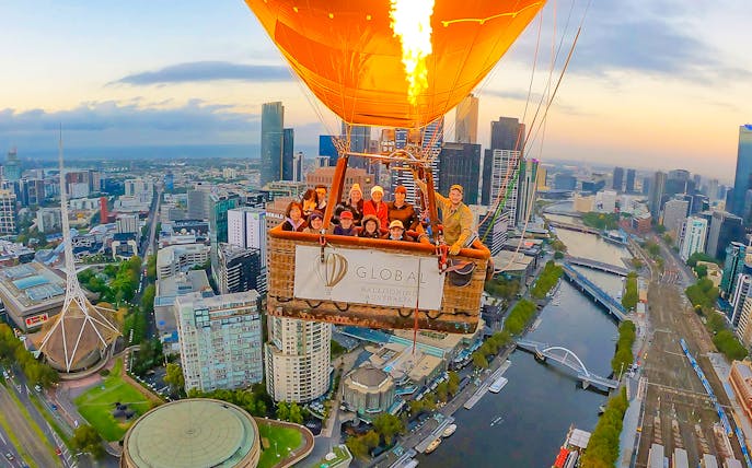 Hot air balloon over Melbourne cityscape at sunrise.