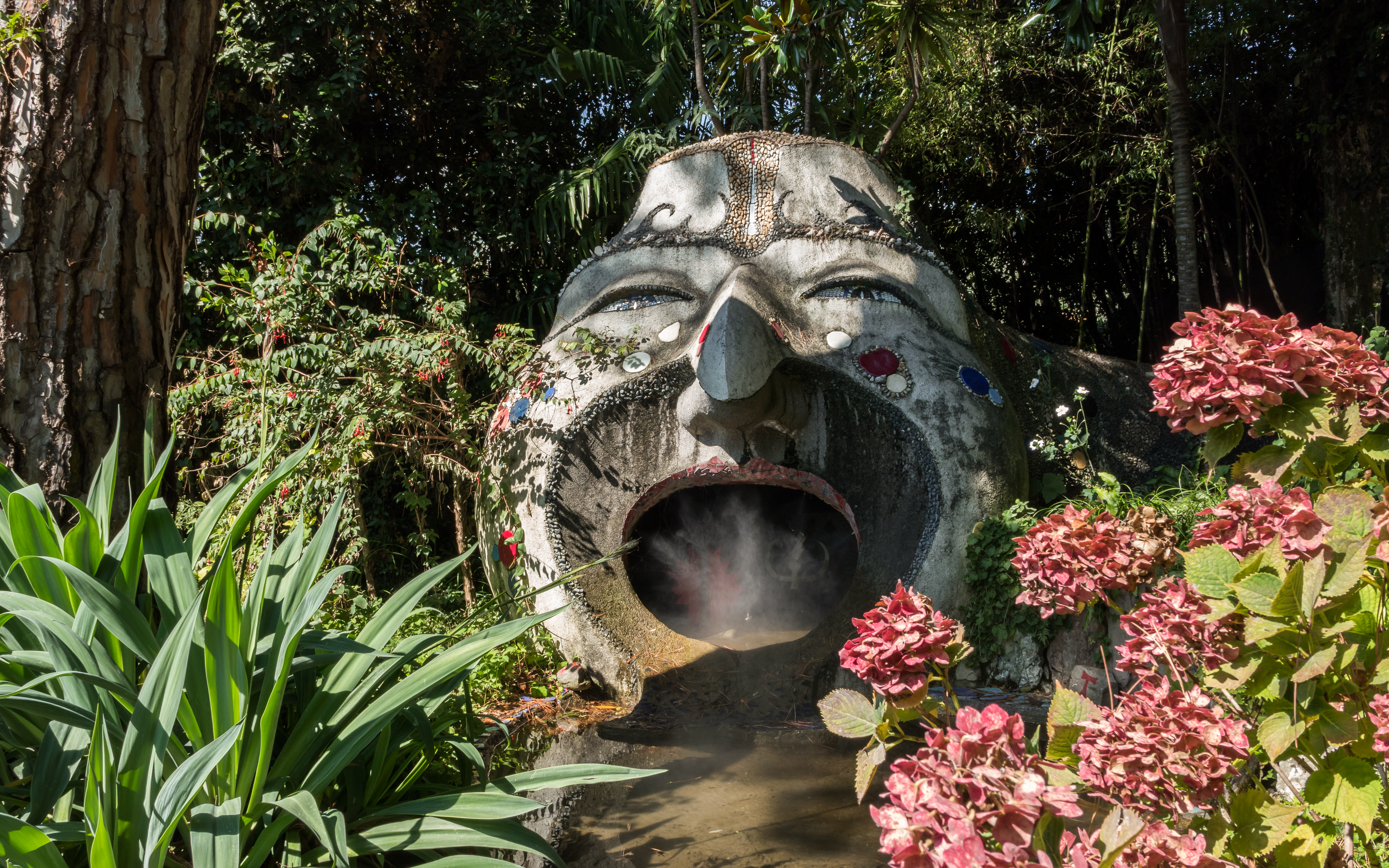 Sculpture with open mouth surrounded by lush plants at ANIMA Garden.
