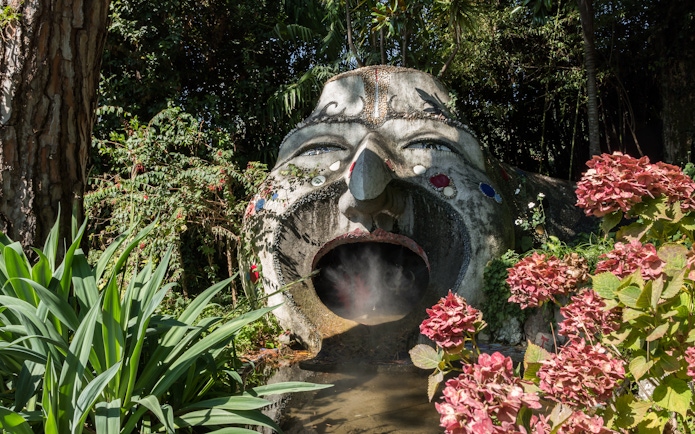 Sculpture with open mouth surrounded by lush plants at ANIMA Garden.