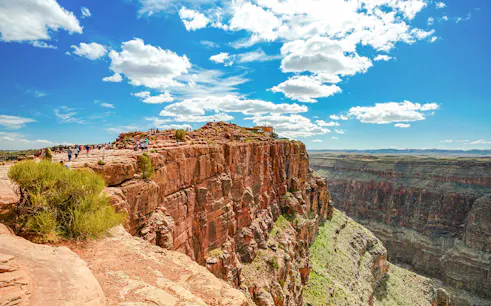 Visitors walking along the edge of Guano Point, Grand Canyon West, under a clear blue sky.