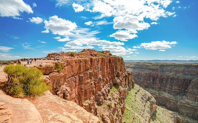 Visitors walking along the edge of Guano Point, Grand Canyon West, under a clear blue sky.