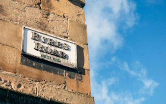 Byres Road street sign in Glasgow's West End under a blue sky.