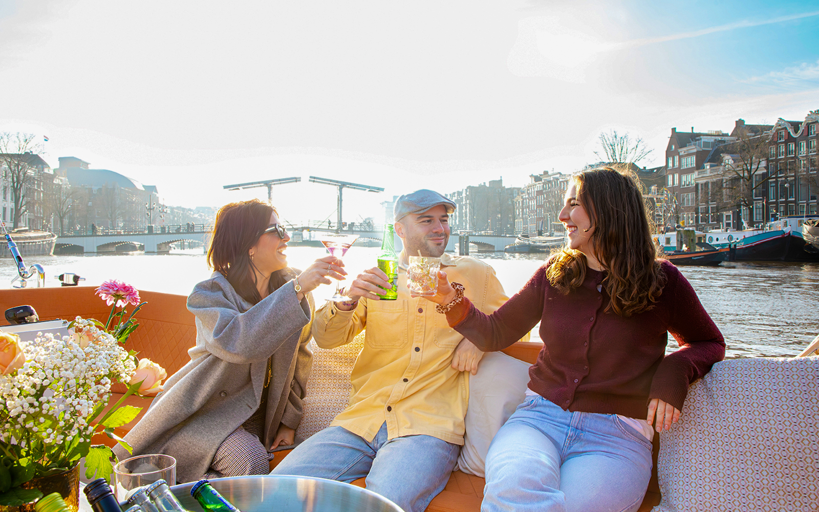 Guests enjoying drinks on an open boat cruise in Amsterdam with canal views.