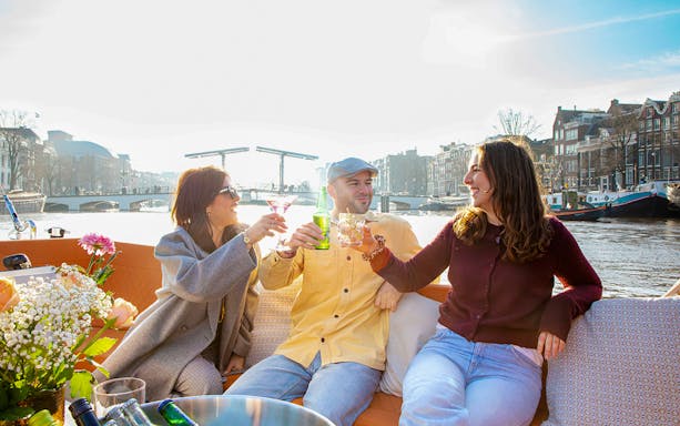 Guests enjoying drinks on an open boat cruise in Amsterdam with canal views.