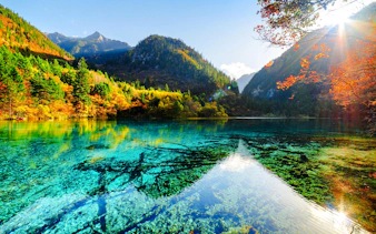 Jiuzhaigou Valley's clear turquoise lake with autumn foliage and mountain backdrop, Chengdu.