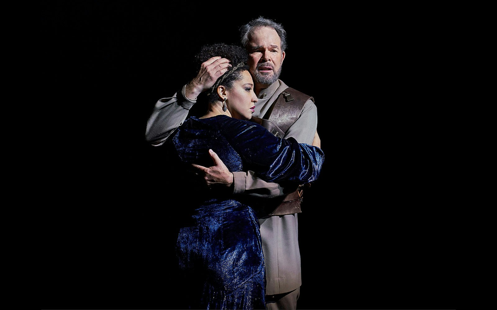 Antony and Cleopatra embrace on stage in dramatic lighting.